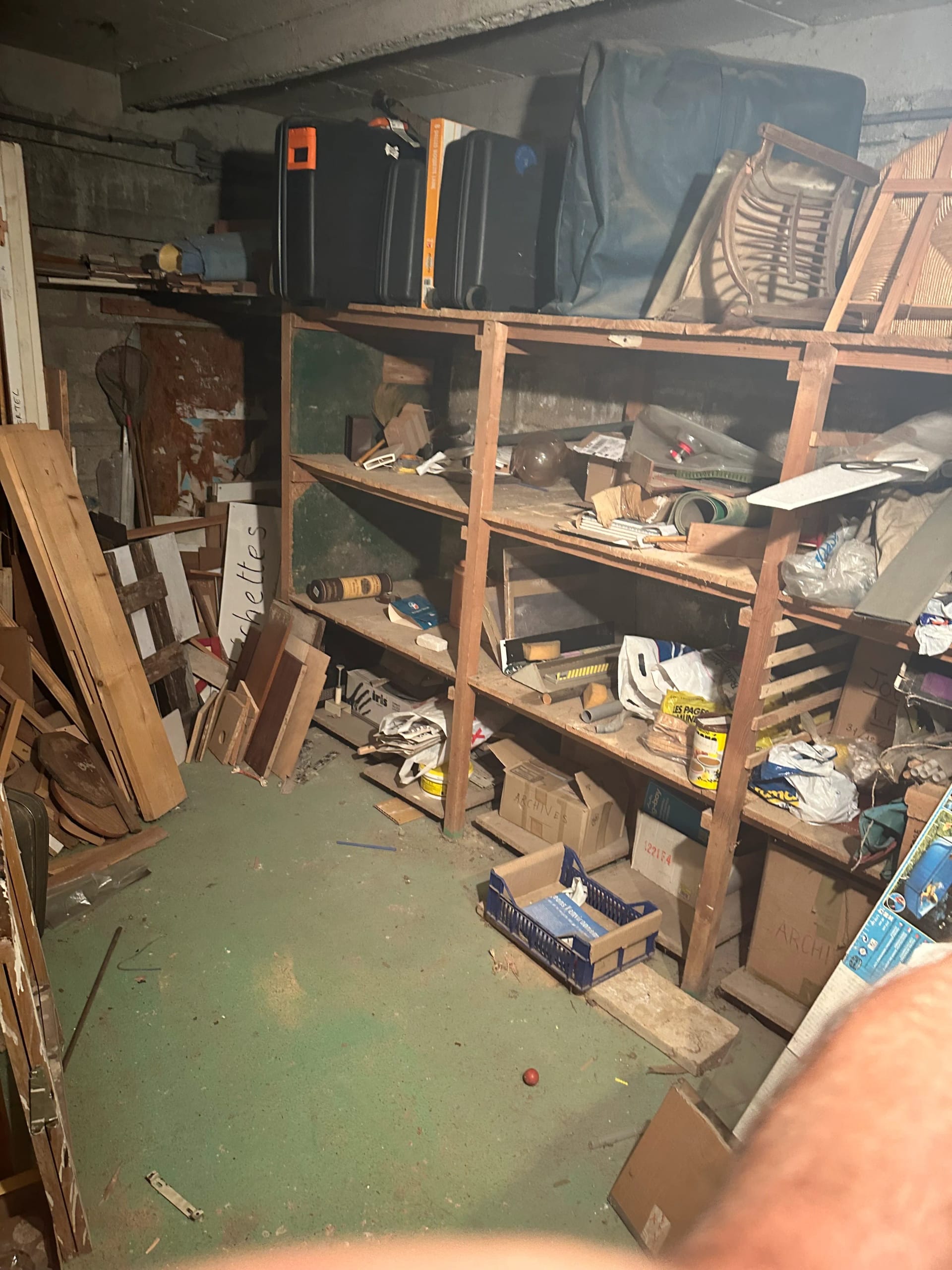 Débarras d'une cave avec étagères en bois et objets divers à Vincennes