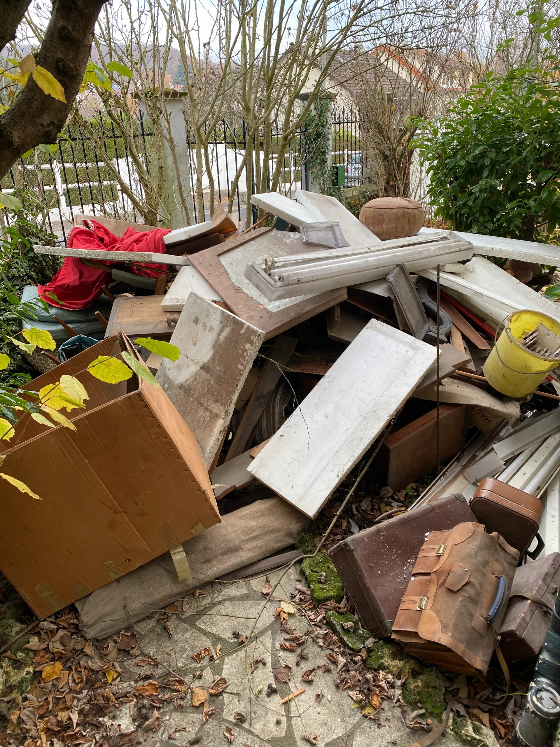 Débarras d'un jardin avec accumulation de débris, planches et vieille valise